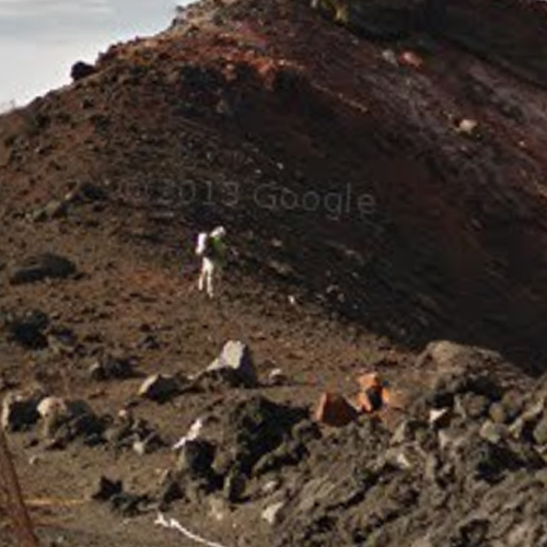 a screenshot of google streetview; a figure in white against a background of rocks. they look like an astronaut. copyright google is across the image
